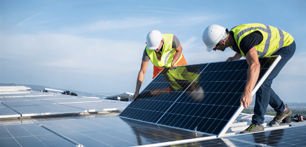 Two workers installing solar panels under a clear sky.