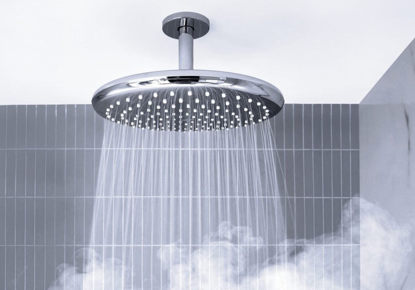 Modern round shower head spraying water in a steamy bathroom.